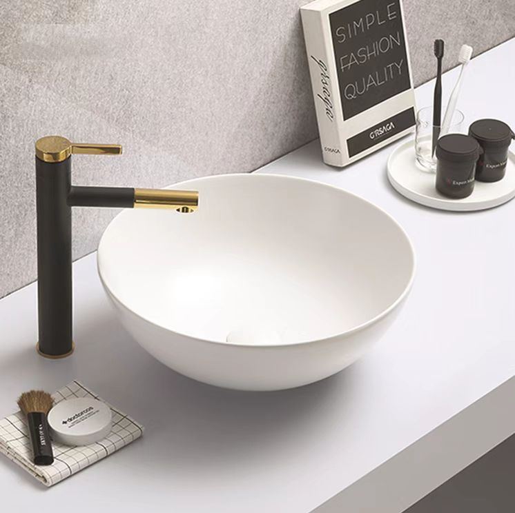 A white above-counter basin with a gold tap